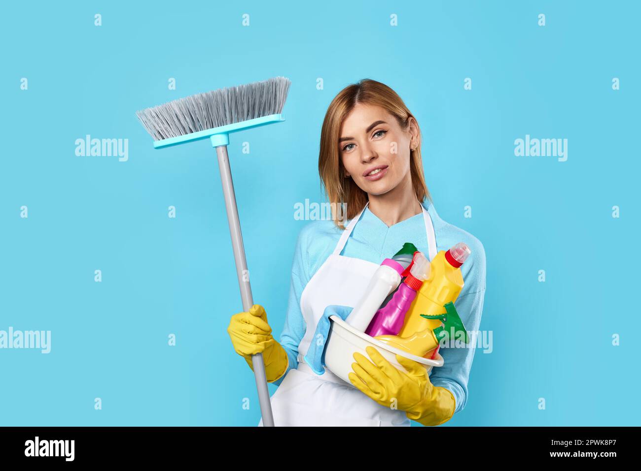smiling blonde woman in yellow rubber gloves and cleaner apron holding ...