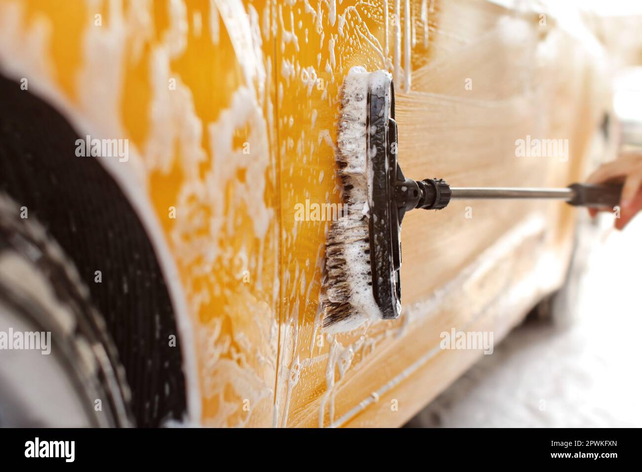 Yellow car washed at self serve carwash, detail on brush cleaning side covered in shampoo foam