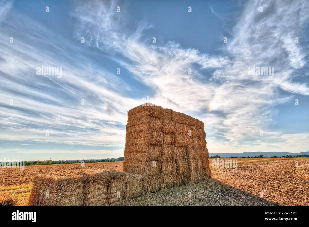 A stack of pressed hay bales on a harvested field with blue sky and ...