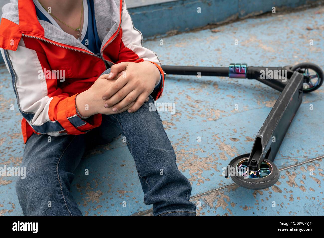 boy holds onto a bruised knee after falling from a stunt scooter Stock ...