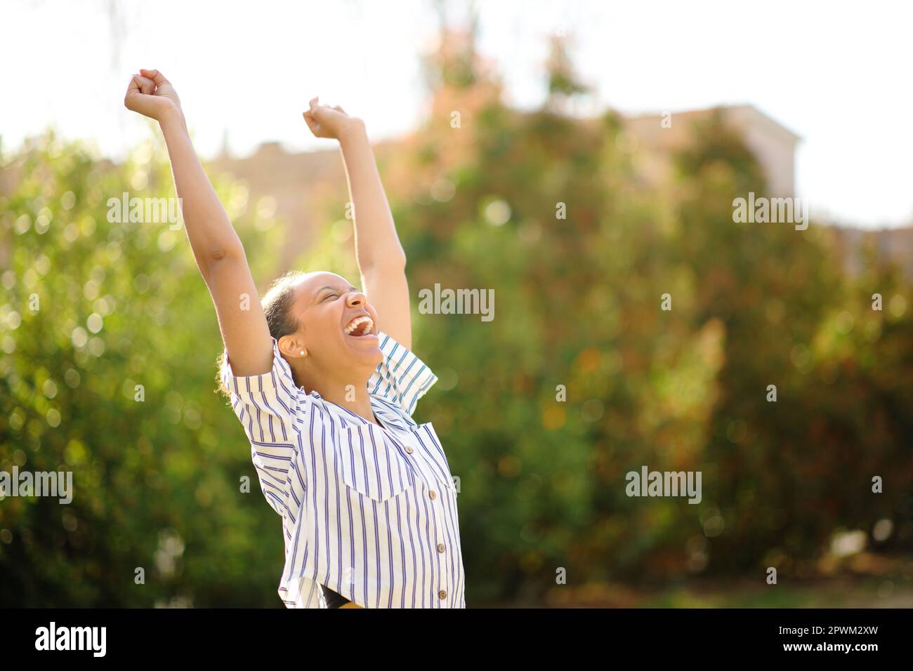 Excited black woman raising arms and screaming in a park Stock Photo