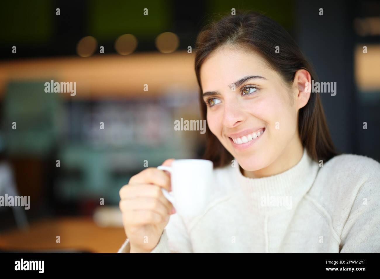 Happy woman smiling looks away holding cup in a coffee shop Stock Photo