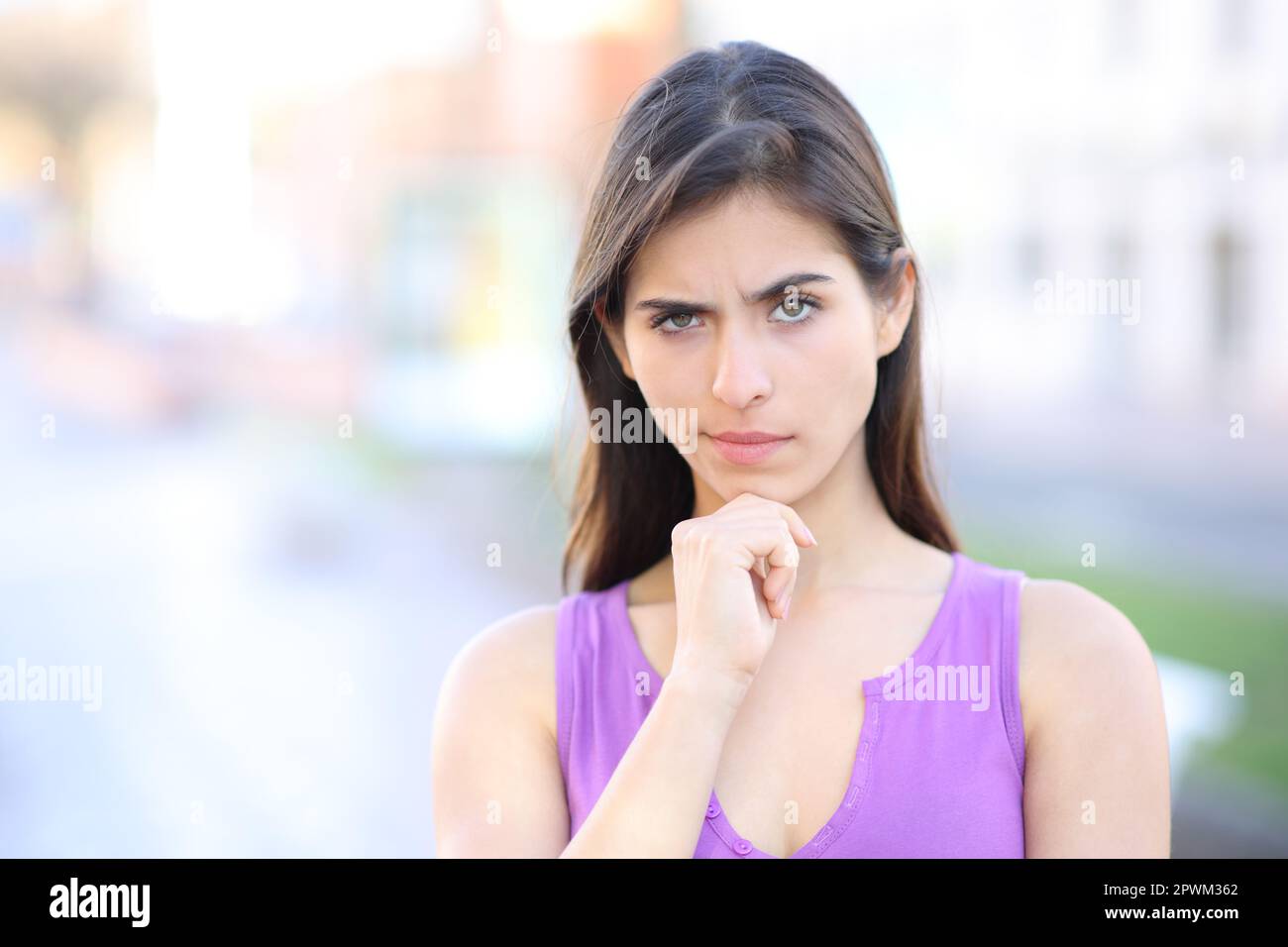 Front view portrait of a suspicious woman looking at camera standing in the street Stock Photo