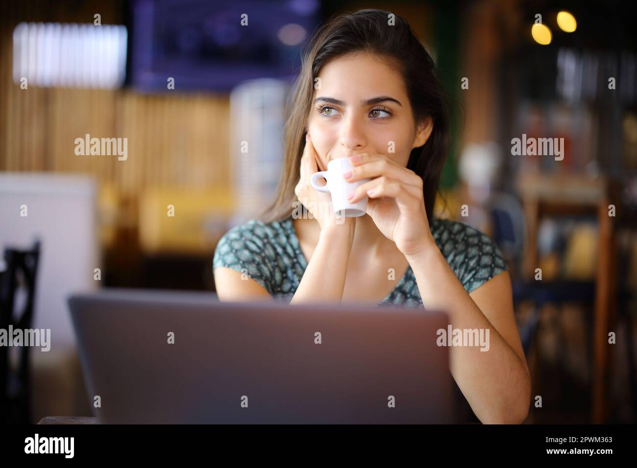 Distracted woman using laptop drinking in a coffee shop looking at side Stock Photo