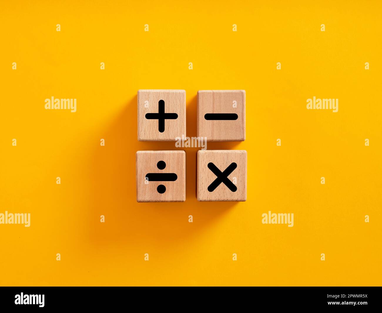 Basic mathematical operations symbols. Plus, minus, multiply and divide symbols on wooden cubes on yellow background. Mathematic or math education and Stock Photo