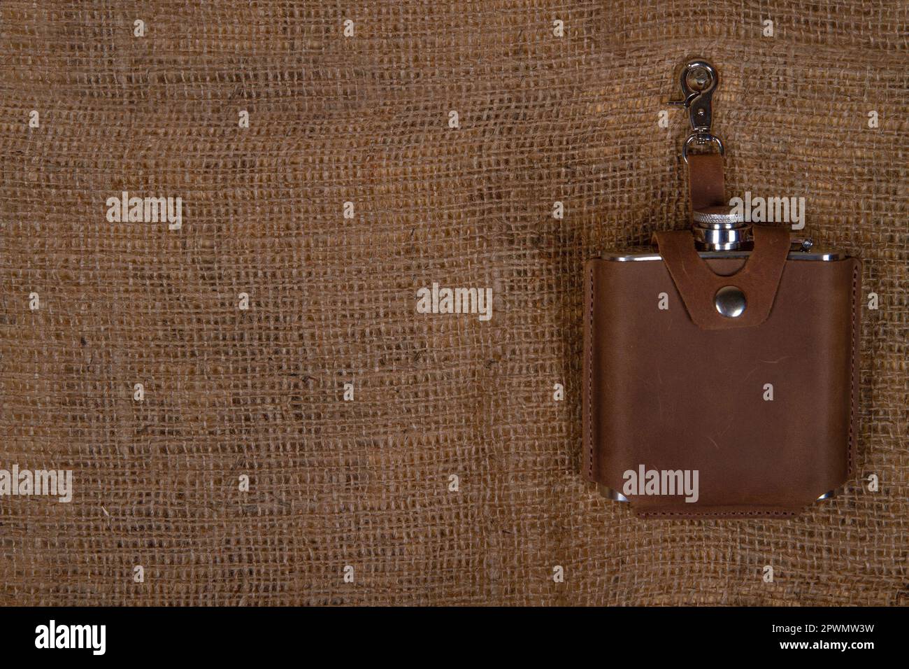 Hip flask in full grain leather case on sackcloth background. Banner with copy space for text place Stock Photo