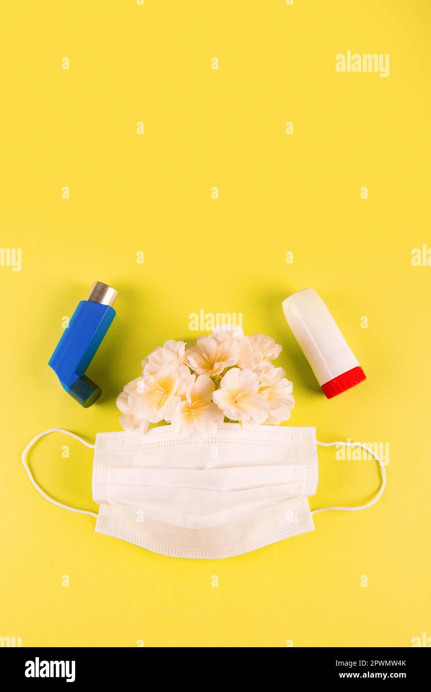 Inhalers, medical mask and spring flowers on yellow background with blank space for text at the top. Concept of Difficulty breathing in caused by alle Stock Photo