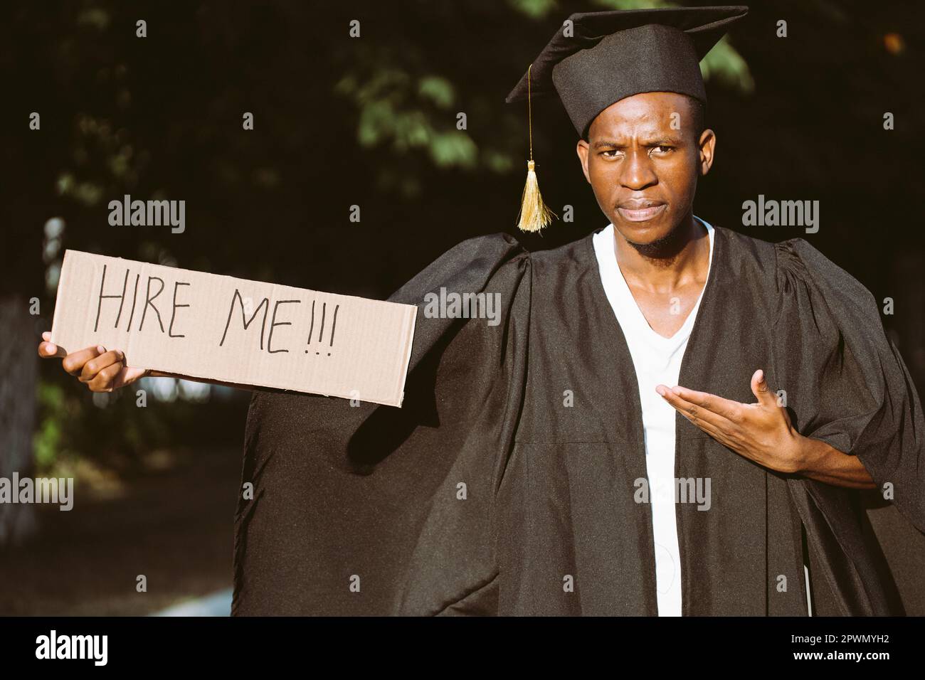 Portrait of black guy standing and pointing at cardboard poster on street in sunny day looking for job. Hiring and employment issue. University or Stock Photo