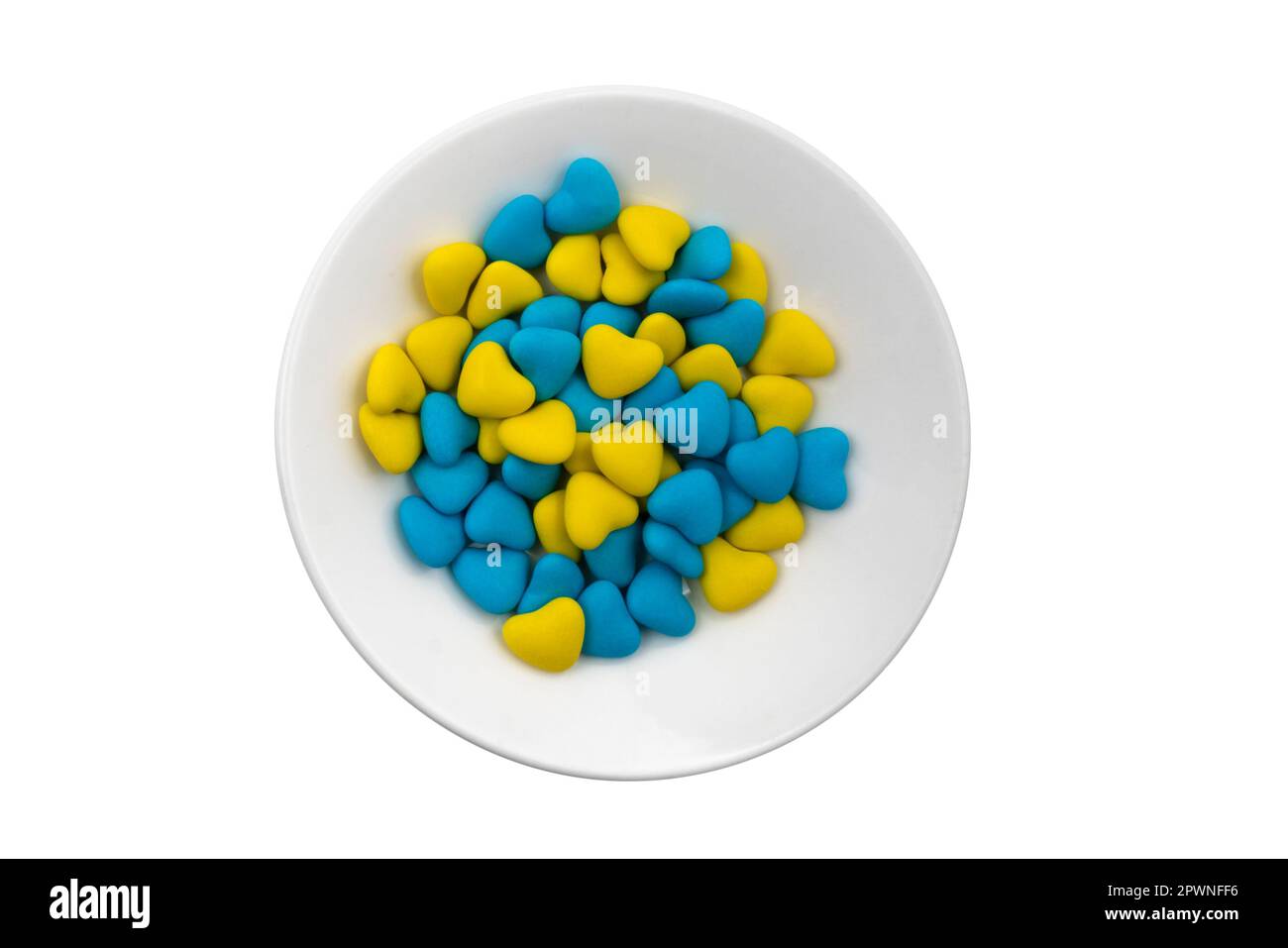 White plate with blue and yellow heart-shaped candies (close-up) isolated on white background. State symbols of Ukraine. View from above Stock Photo
