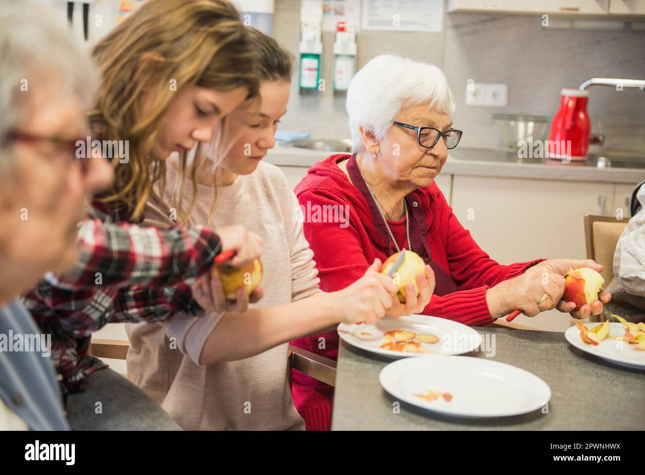Senior women with girls peeling apple at rest home Stock Photo