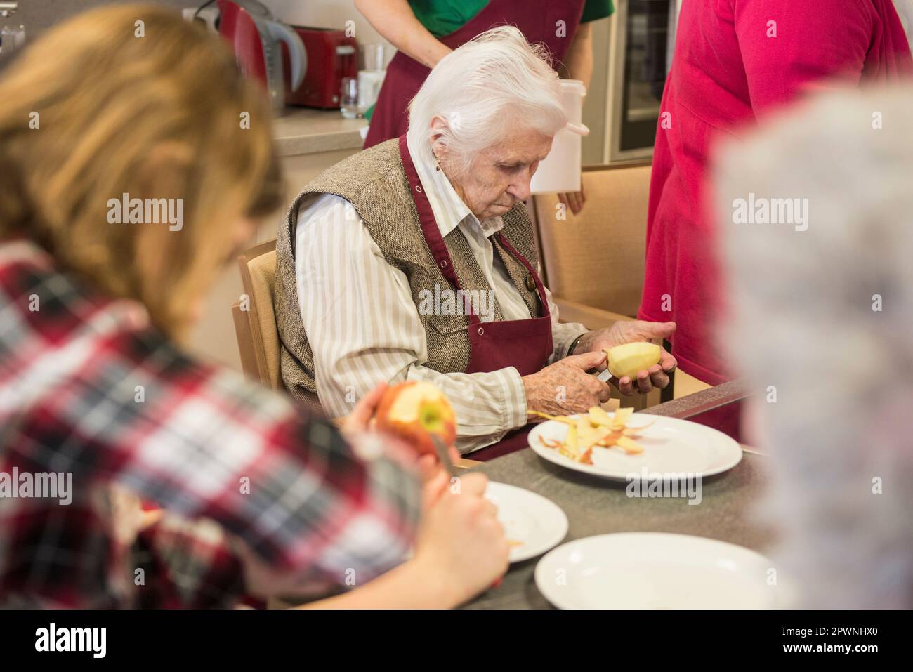 Senior women with girls peeling apple at rest home Stock Photo