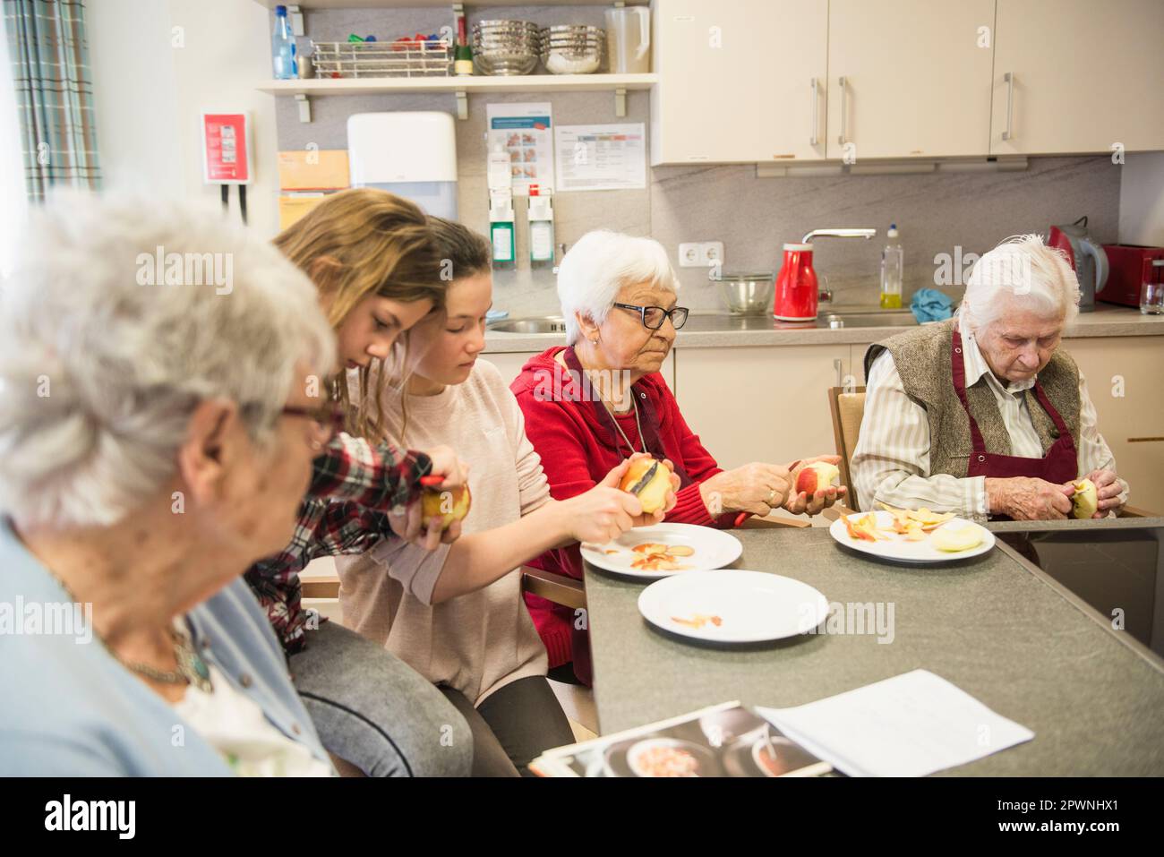 Senior women with girls peeling apple at rest home Stock Photo