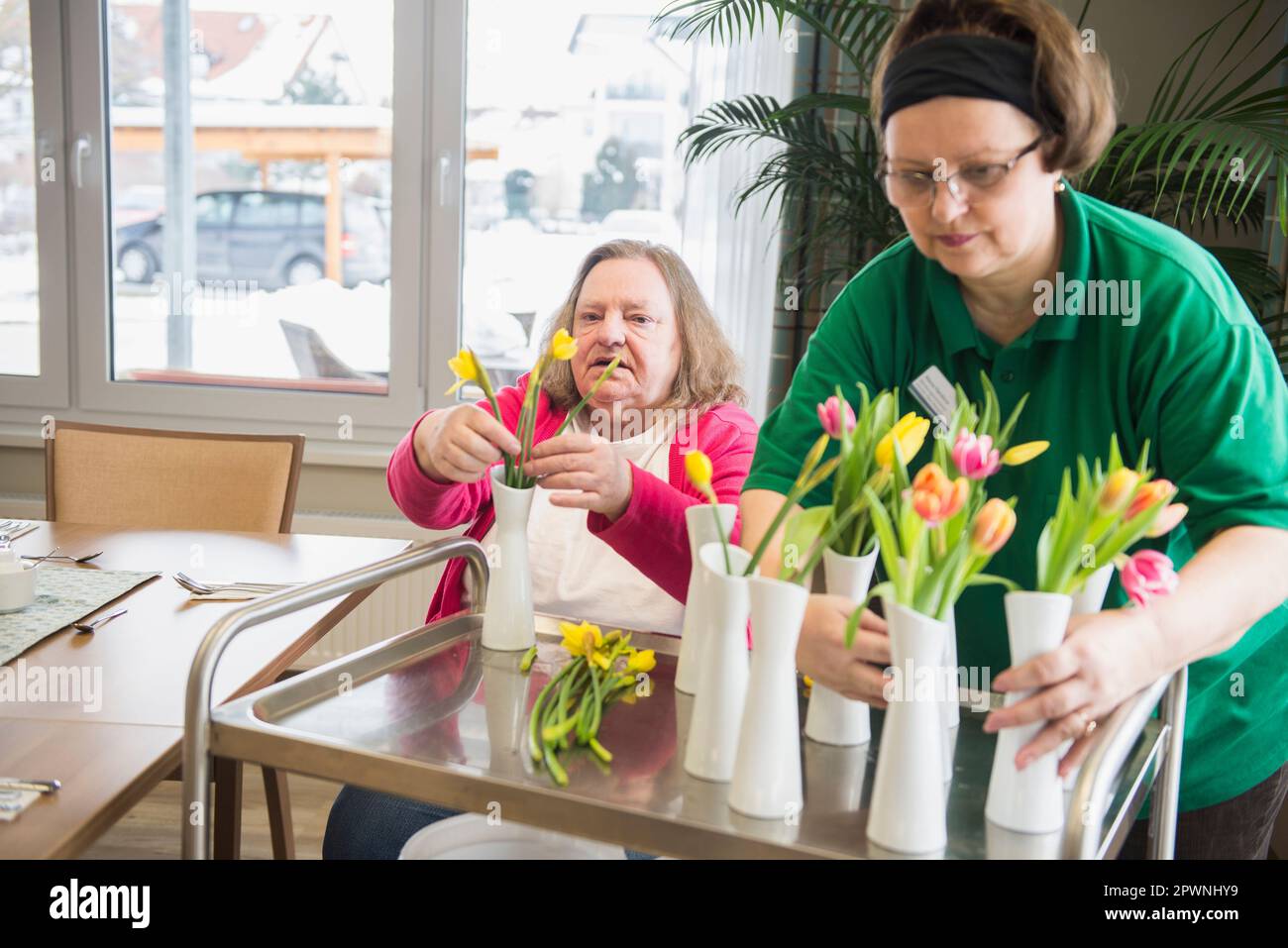 Caretaker and senior woman arranging flowers and vases at rest home Stock Photo