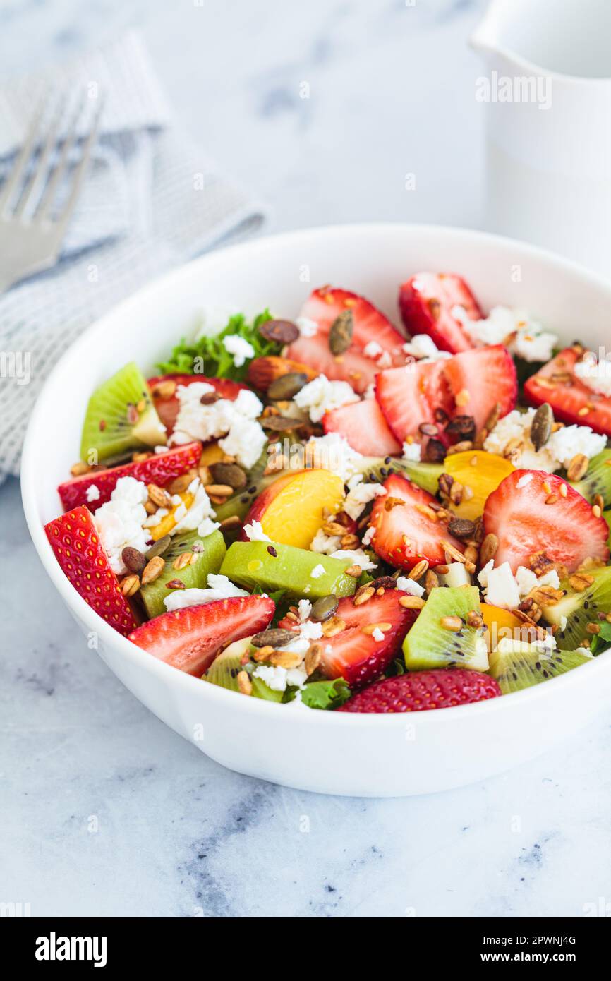 Fruit salad with feta and seeds in a white bowl on a white table. Healthy vegan detox summer recipe. Stock Photo