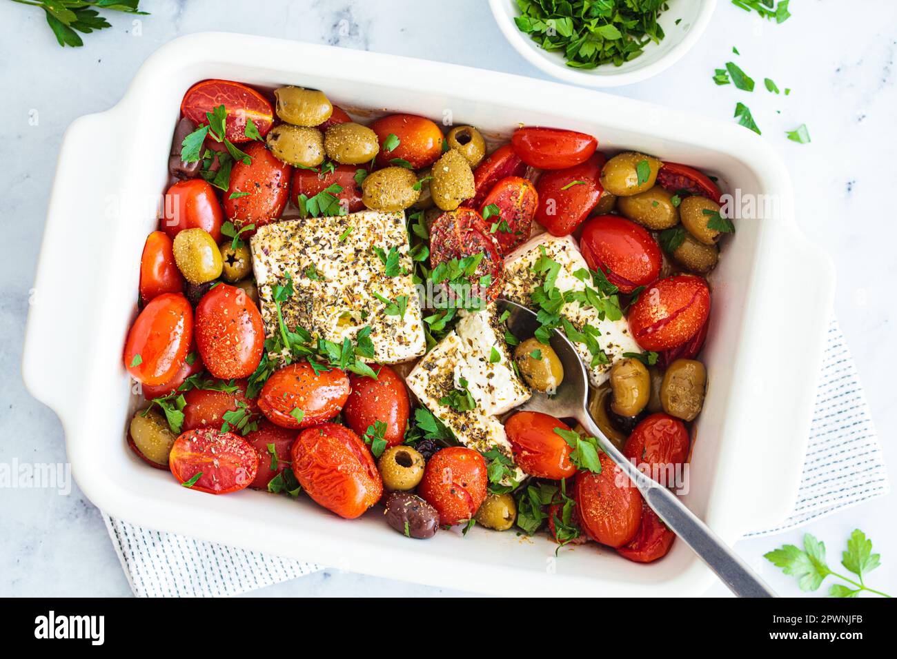 Baked feta cheese with cherry tomatoes and olives on a white table, top view. Stock Photo