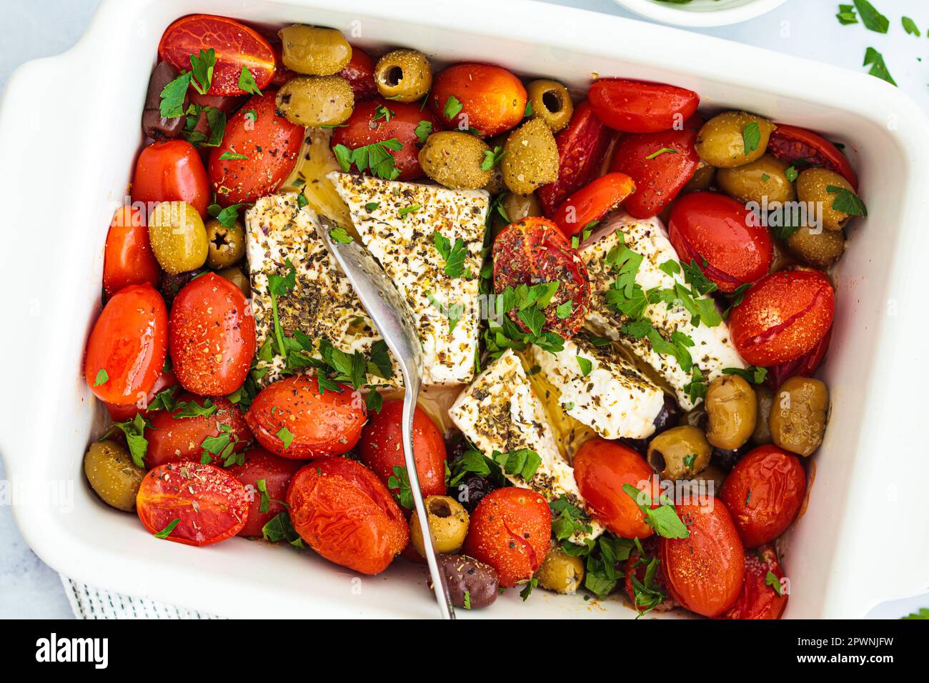 Baked feta cheese with cherry tomatoes and olives on a white table, top view. Stock Photo