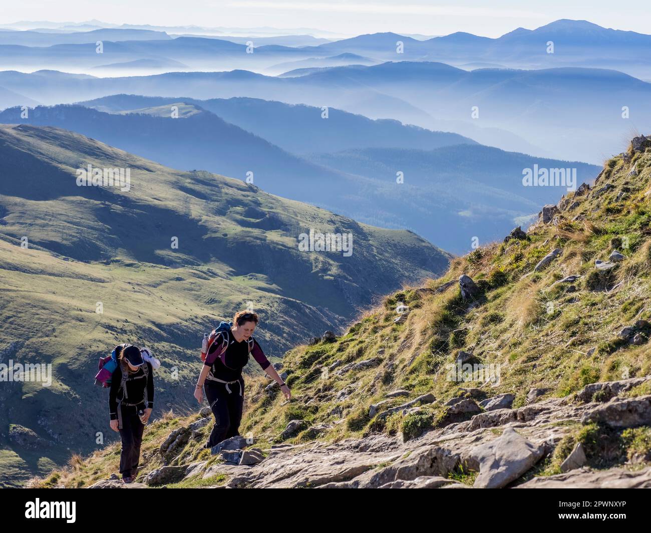 Two women walking towards the top of Txindoki during hiking tour Stock Photo