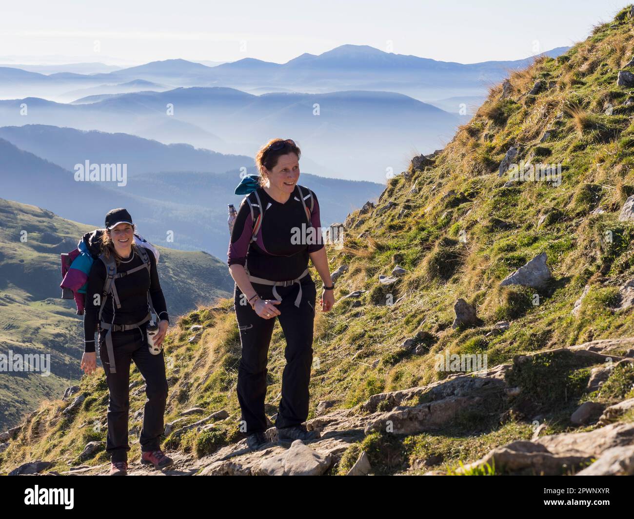 Two women walking towards the top of Txindoki during hiking tour Stock Photo
