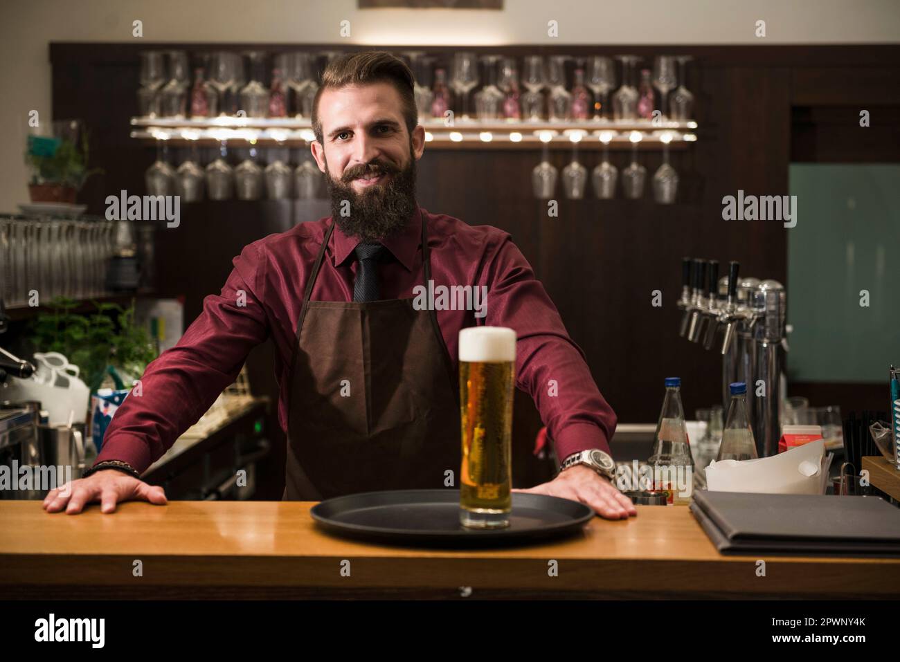 Portrait of young man at bar counter with glass of beer in tray Stock Photo