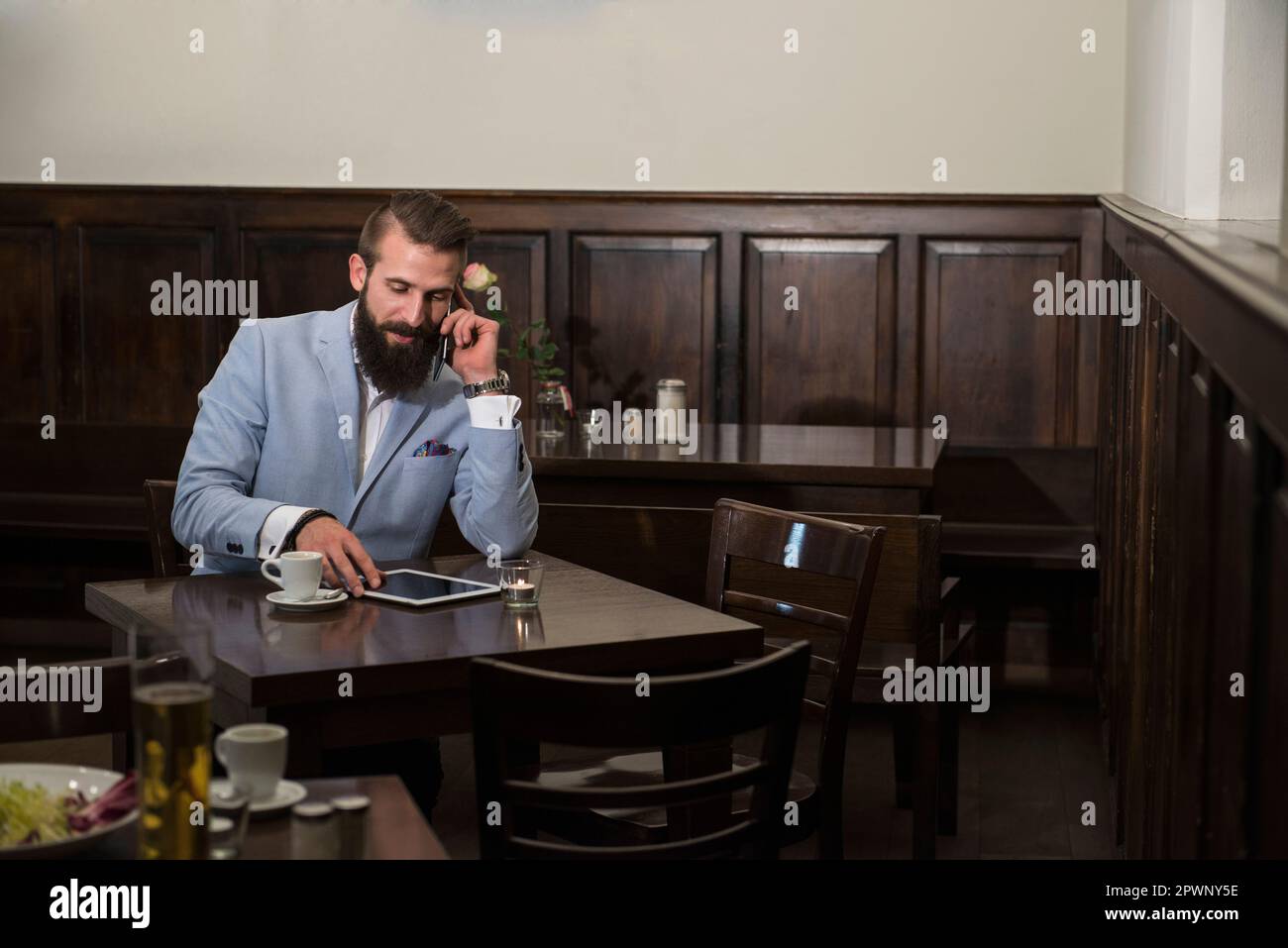 Young man talking on phone while using digital tablet at restaurant Stock Photo