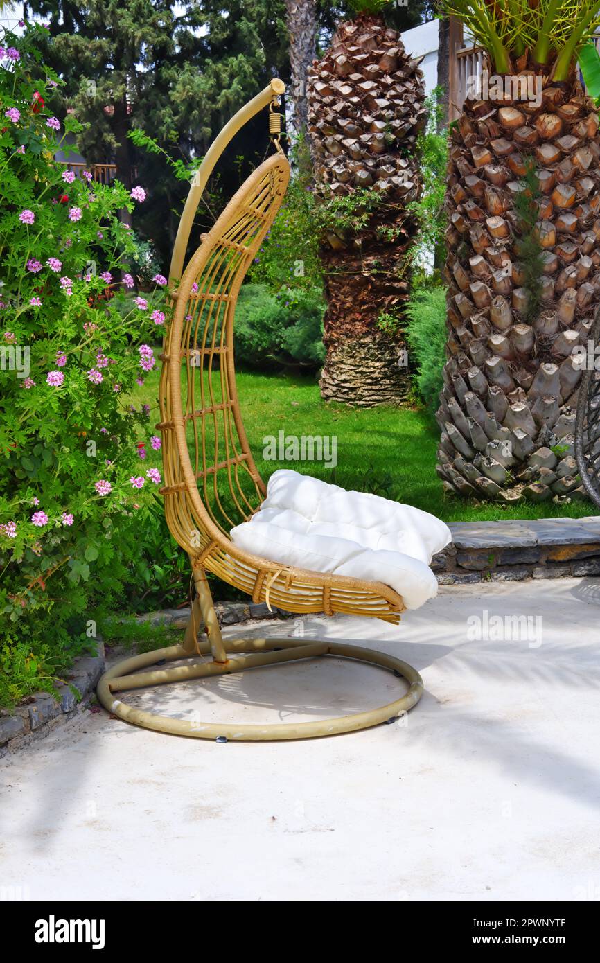 Bambu chairs outdoor at garden with beautiful flowers and palm trees in summer. Also with white summer houses at the background Stock Photo