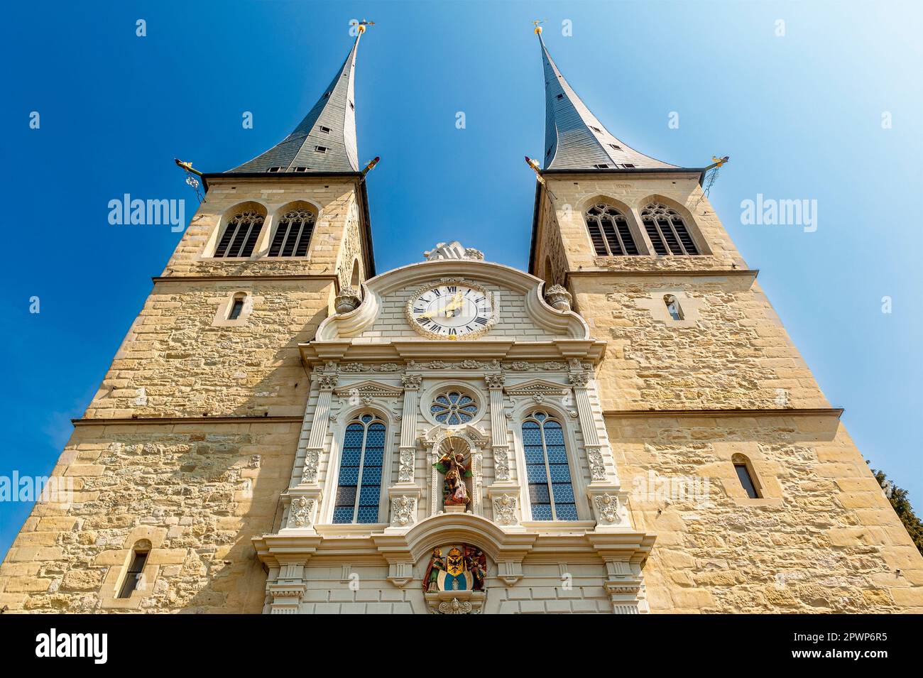 Frog perspective of the front side of the Catholic Court Church of St. Leodegar in Lucerne with its two towers and a clock with clock face in sunshine Stock Photo