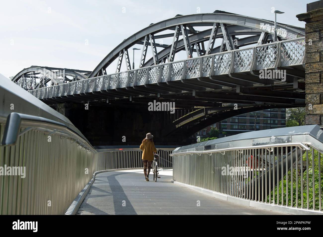 a woman pushes a bicycle on dukes meadows footbridge, below barnes bridge on the river thames, chiswick, london, england Stock Photo