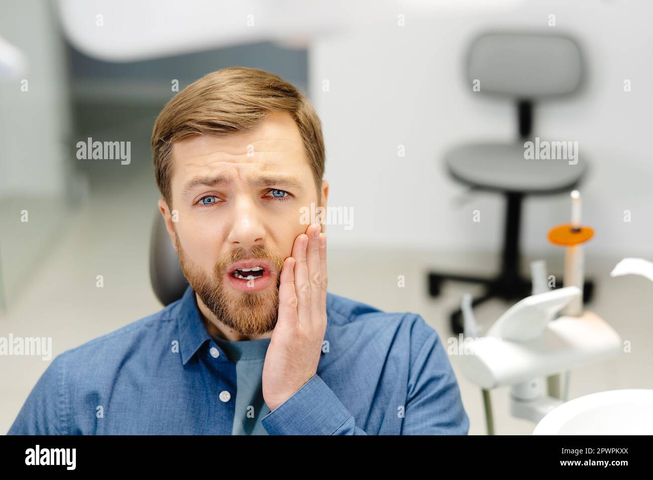 Sad man sitting in dental chair suffering from acute tooth pain