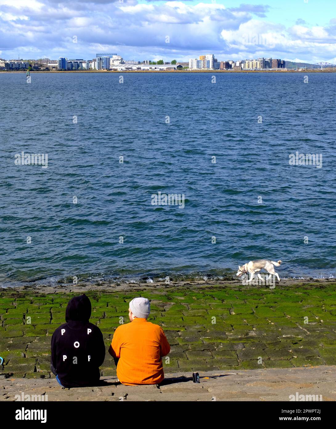 Edinburgh, Scotland, UK. 1st May 2023. Making the most of the Bank Holiday chilling out on the Forth Estuary breakwater at Newhaven after a mild but mostly cloudy start to the day. View towards Granton harbour and modern development.  Credit: Craig Brown/Alamy Live News Stock Photo