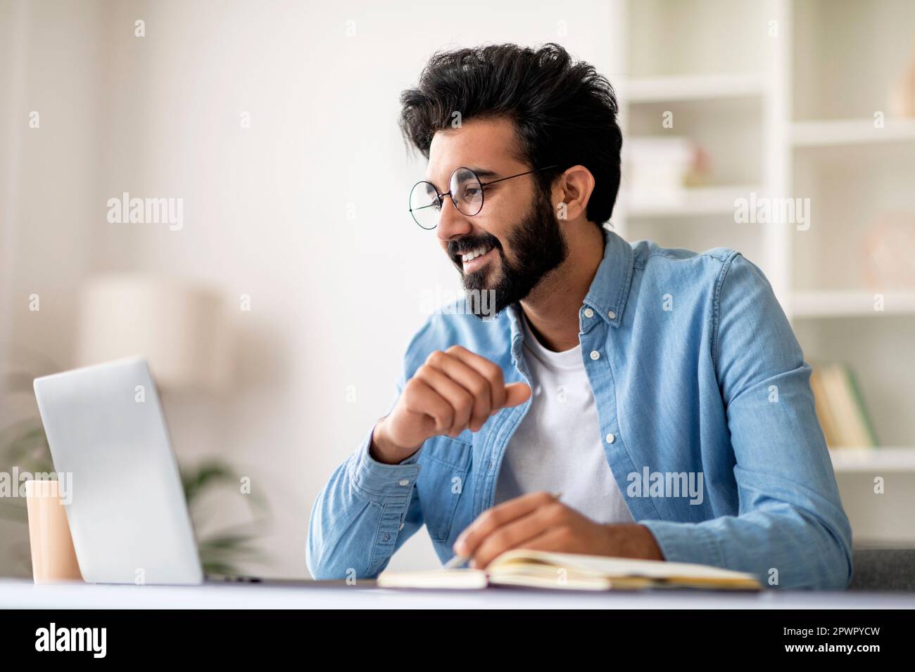 Indian man using laptop and taking notes while working at home office Stock Photo