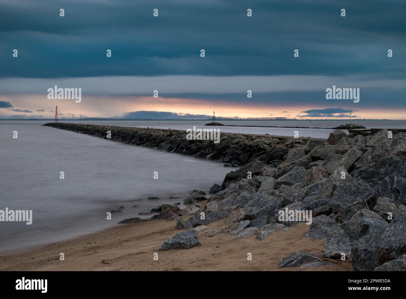 Rocky pier and threatening dark clouds during sunset at Playa Sere, Colonia, Uruguay Stock Photo
