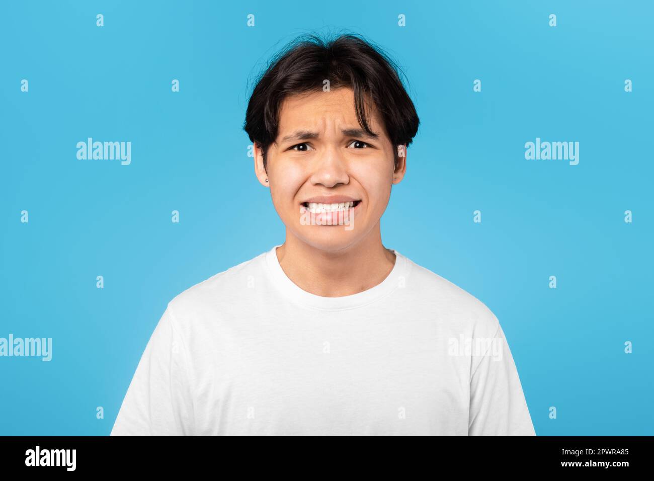 Disgusted Asian Teen Guy Grimacing Looking At Camera, Blue Background Stock Photo