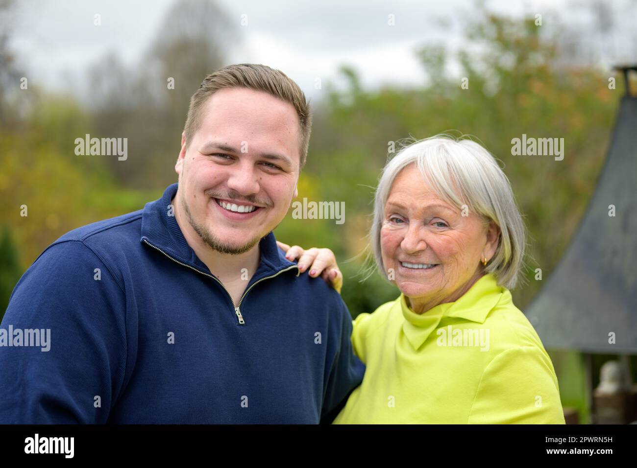 Two generation family, grandmother and grandson standing next to each other laughing and Grandmother has her hand on his shoulder Stock Photo