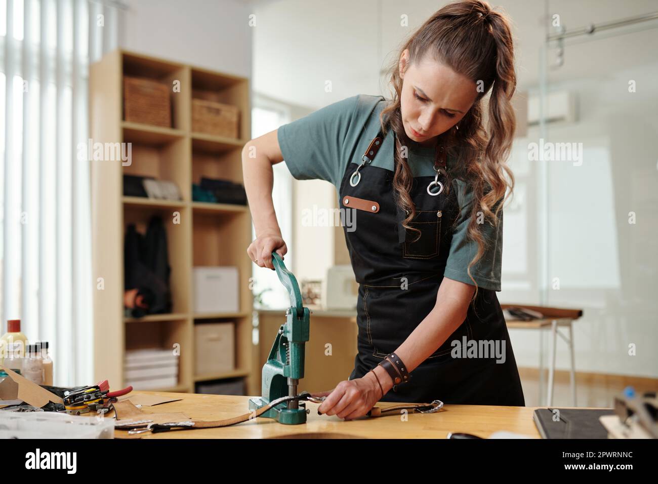 Leather worker using hand press when making holes in leather bag handle Stock Photo