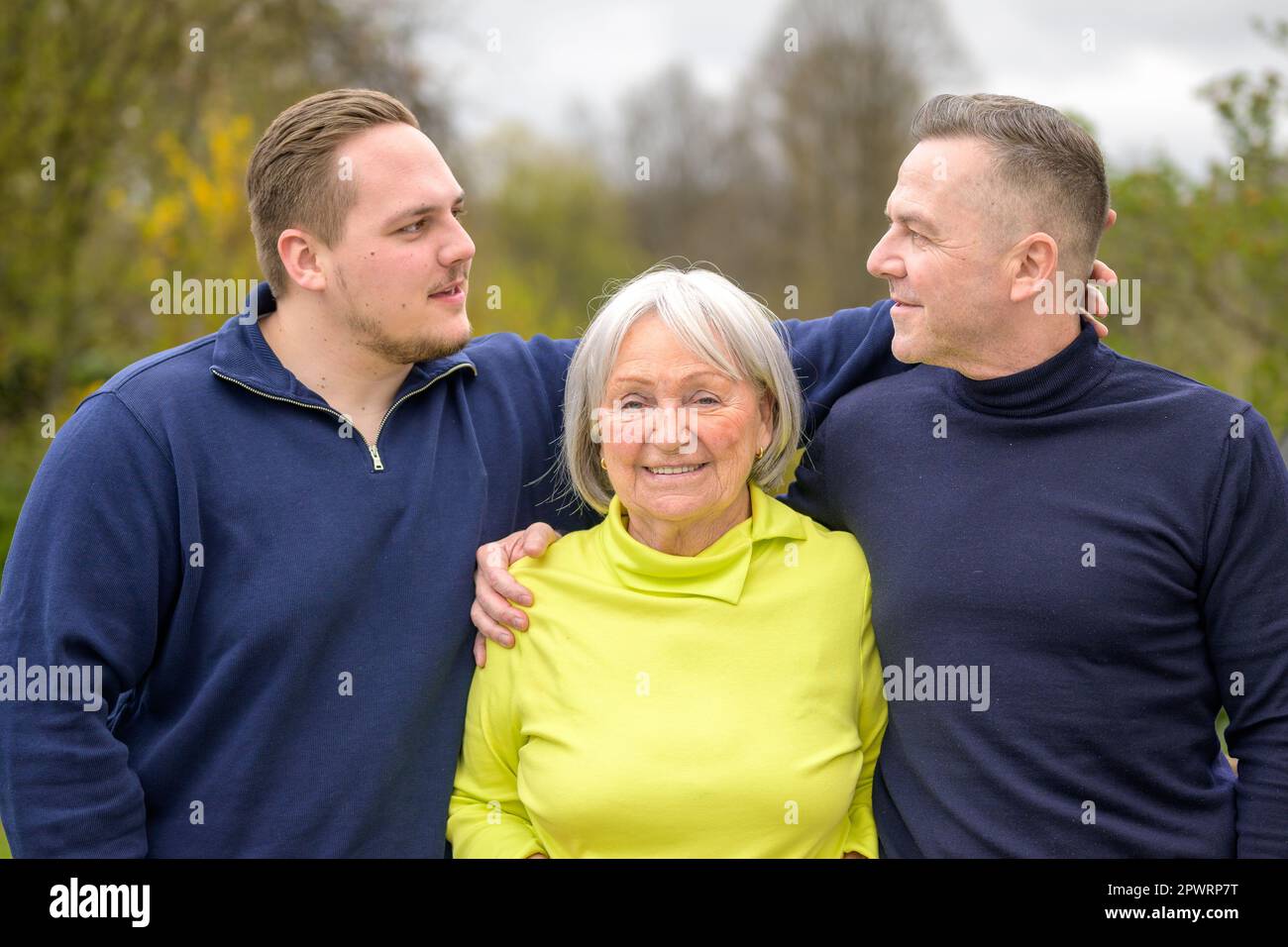Three generation family, grandmother, son and grandson hold each other's arms and father and son look at each other Stock Photo