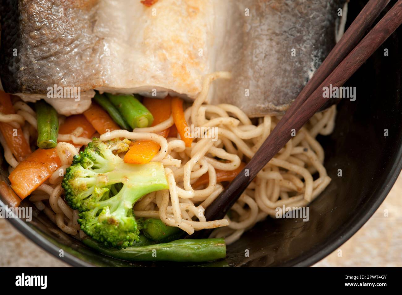 Serving of milkfish with noodles and fresh vegetables in a bowl with chopsticks in a cropped overhead close up view Stock Photo