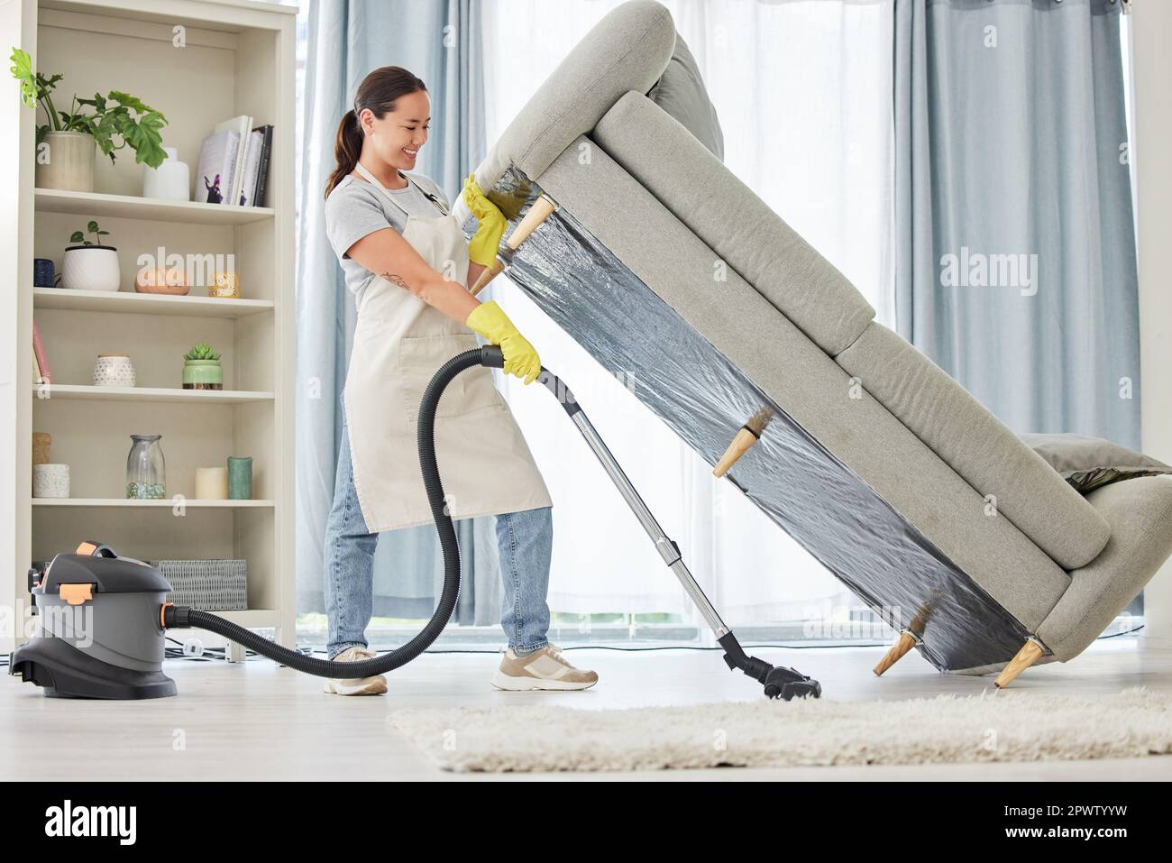 A mixed race domestic worker lifting and cleaning under the sofa. One