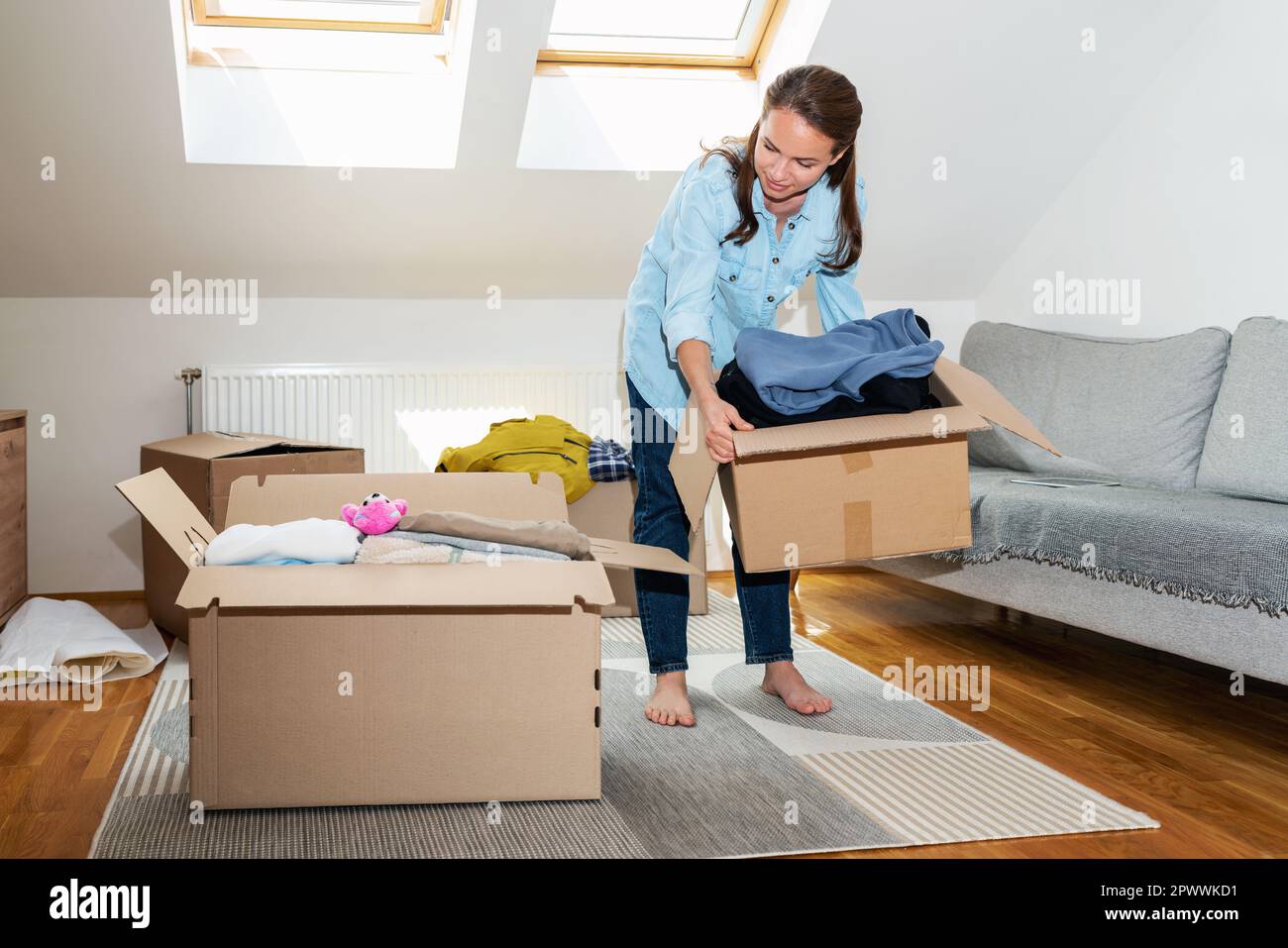 Woman packing her clothes in cardboard boxes, moving house concept