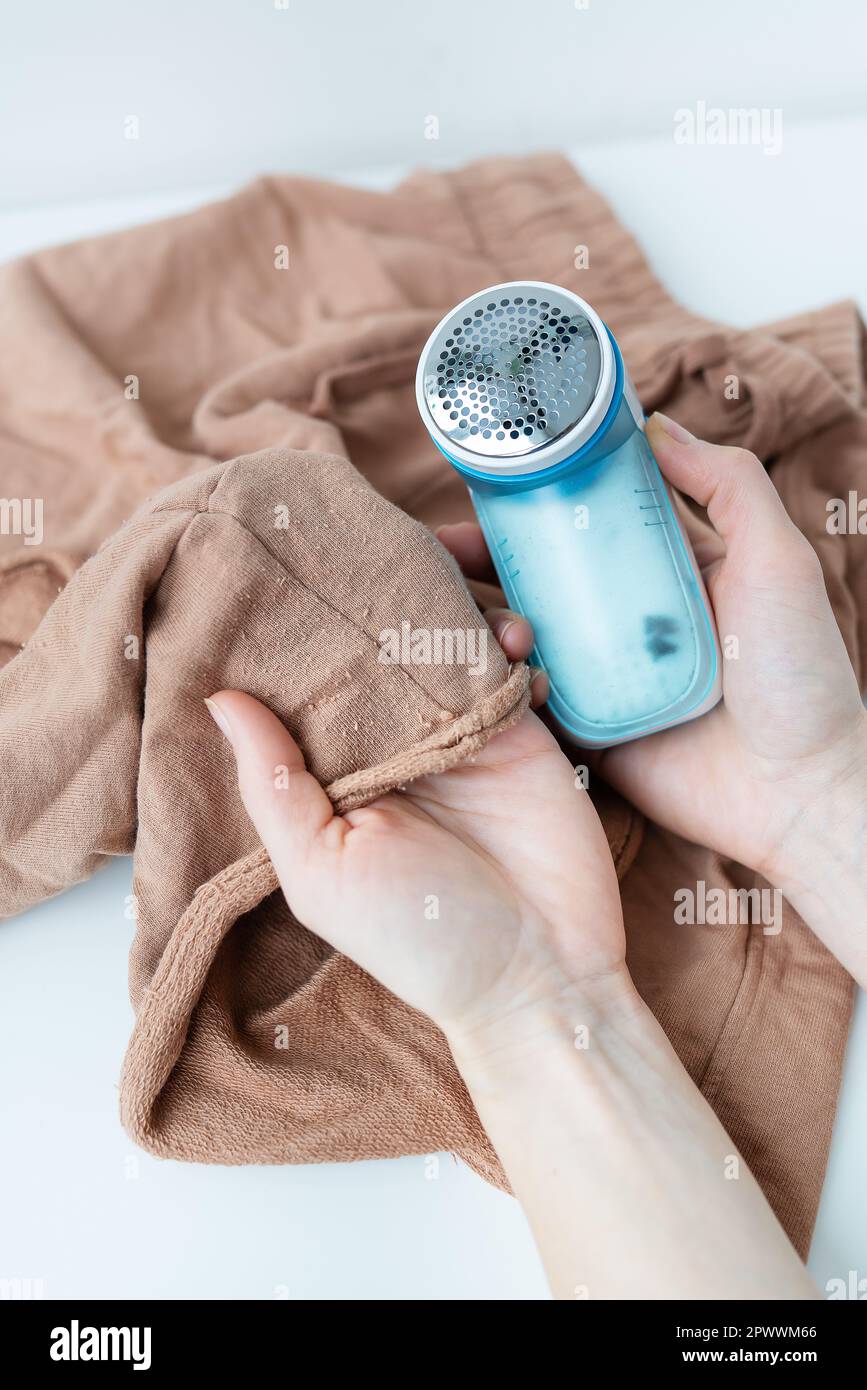 A girl removes large coils from clothes using an electronic machine. The concept of saving clothes, cleaning from coils Stock Photo