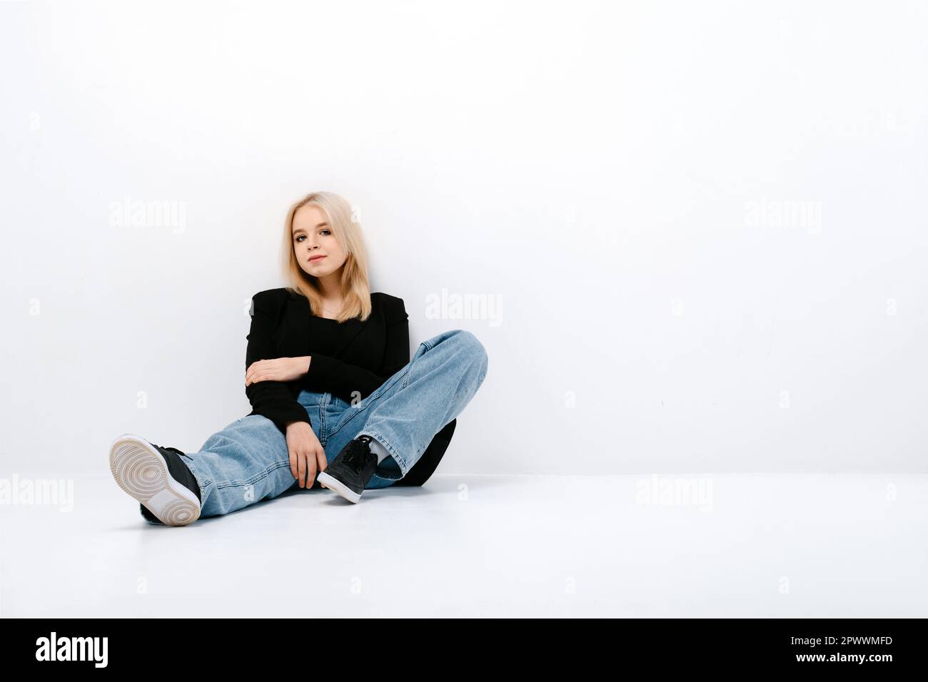 Cute girl in tank top, jacket and jeans posing sitting on the floor in
