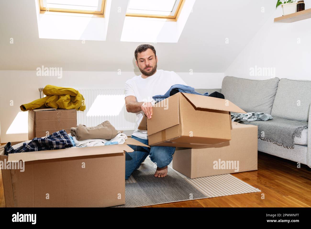 Volunteer man packing his old apparel into cardboard boxes at home, reusing, second hands concept. Stock Photo