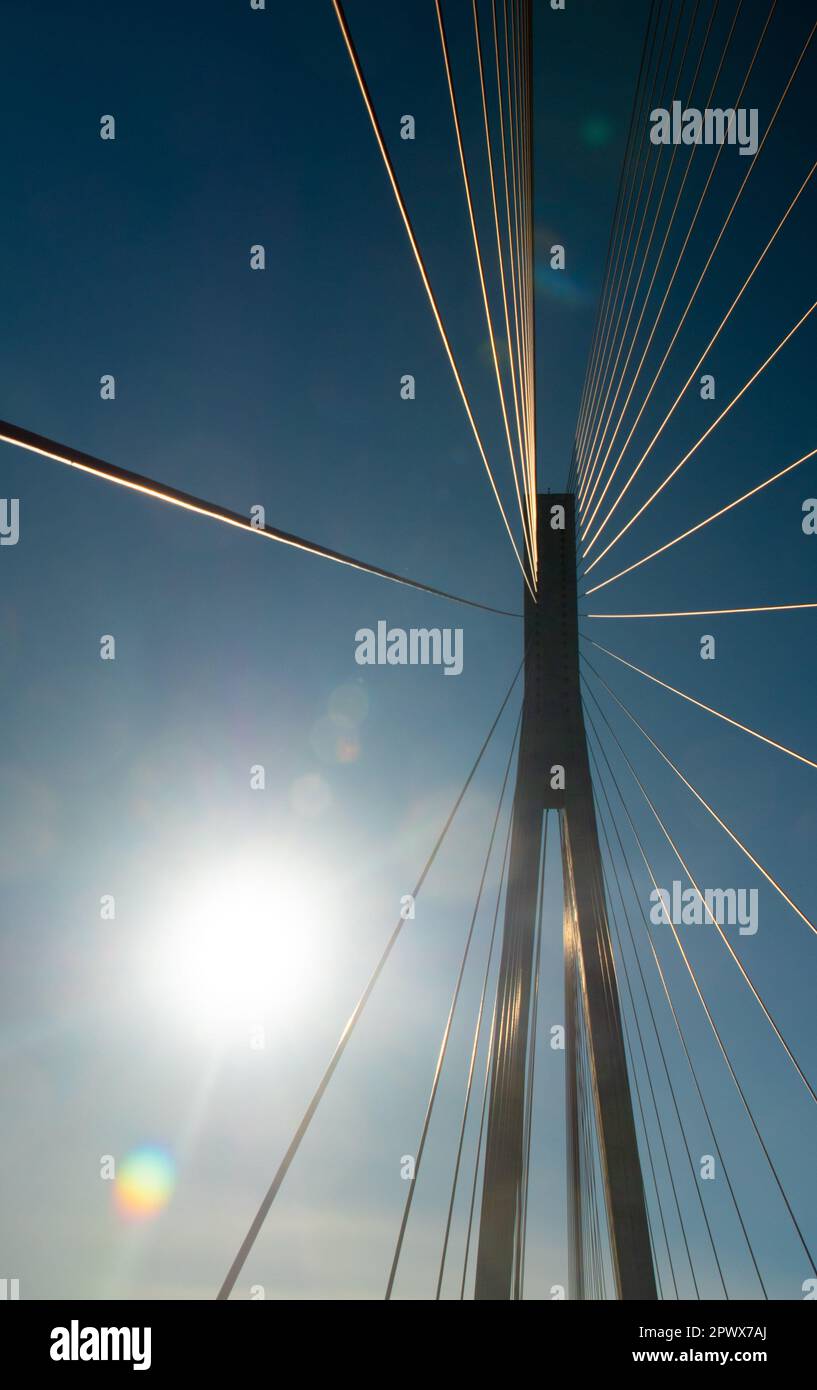 Support and cables of the suspension bridge against the background of the blue sky and the glare of the sunbeam Stock Photo