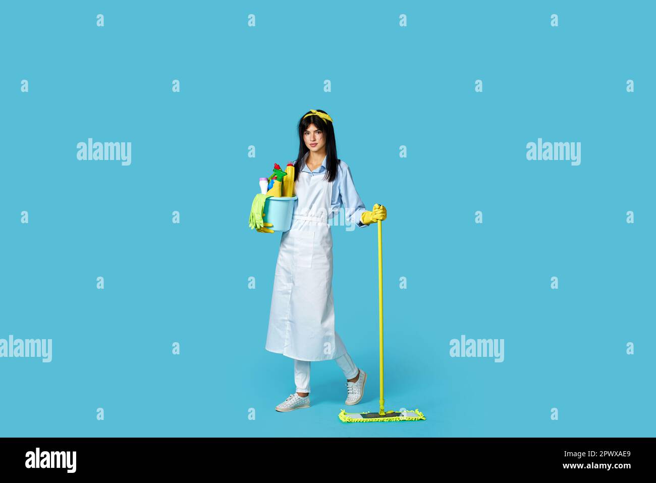 pretty woman in rubber gloves and cleaner apron with cleaning supplies ...