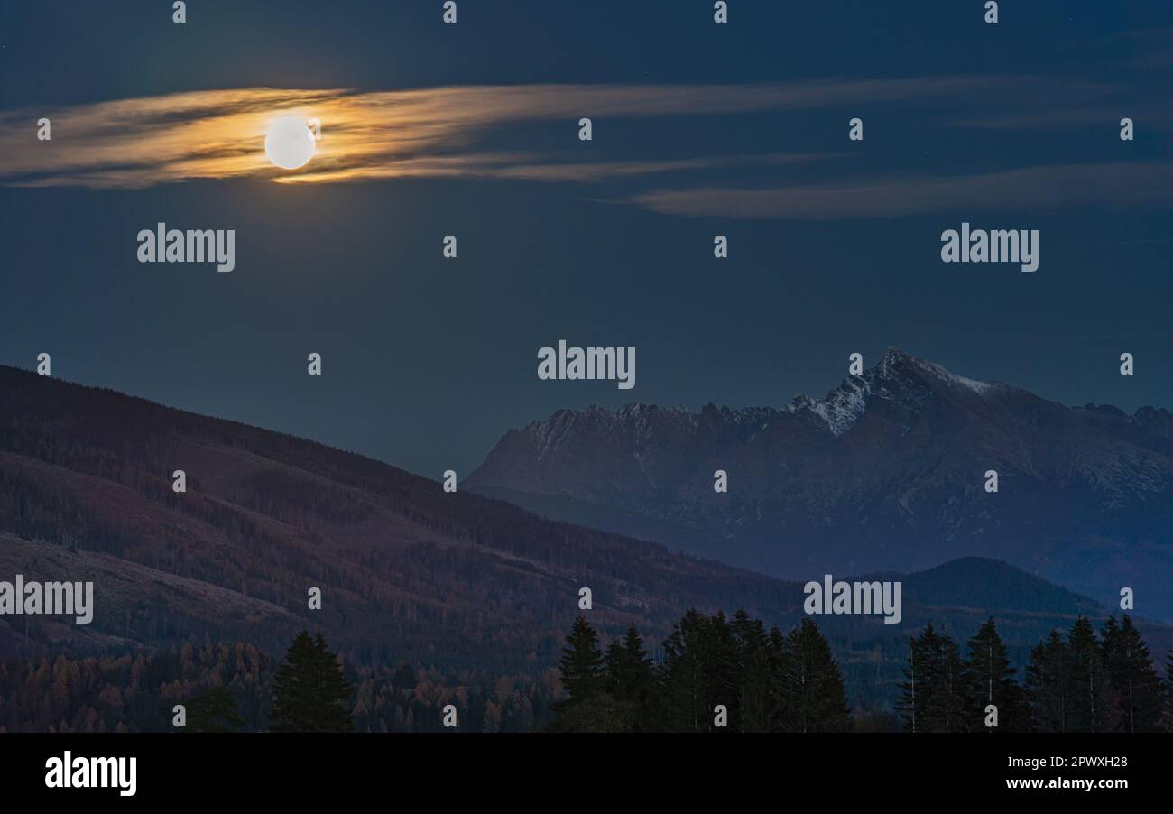 Full moon over mount Krivan peak - Slovak symbol - forest trees silhouettes in foreground, evening photo. Stock Photo