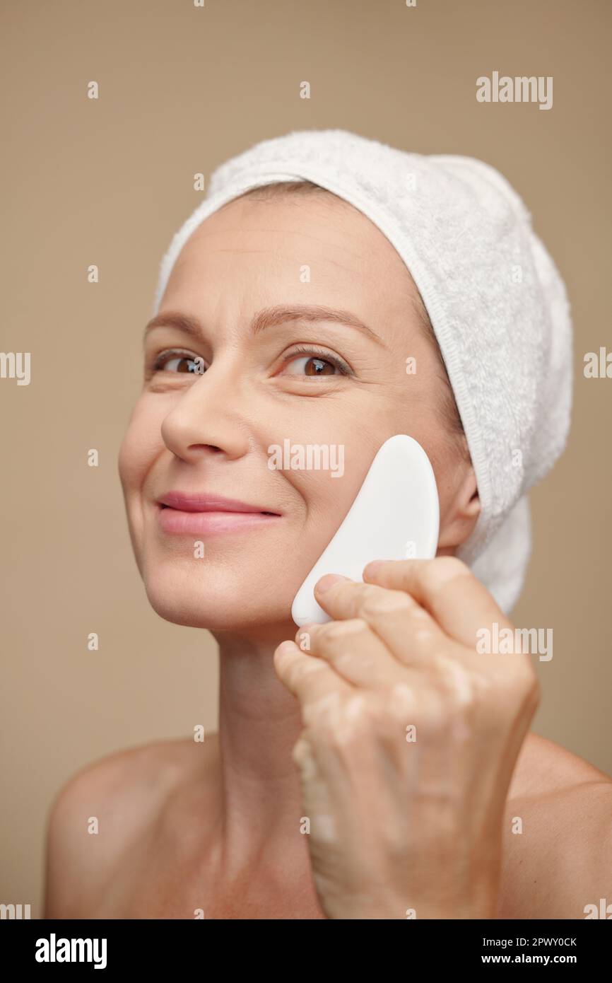 Happy middleaged woman massaging face with gua sha after morning