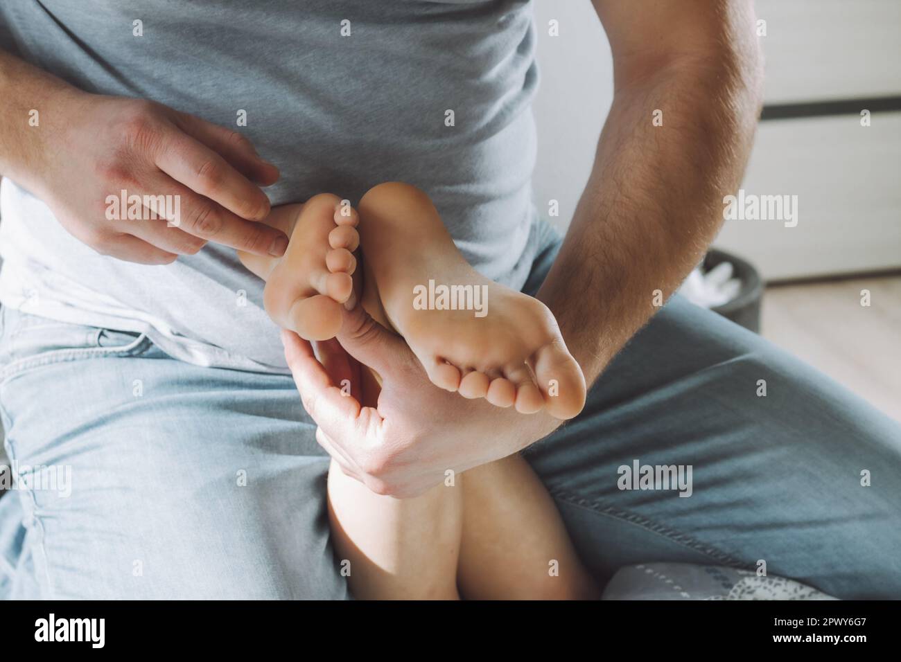 Children's feet in hands of father. Dad tickles feet of kid sitting on them. Family having fun at home Stock Photo