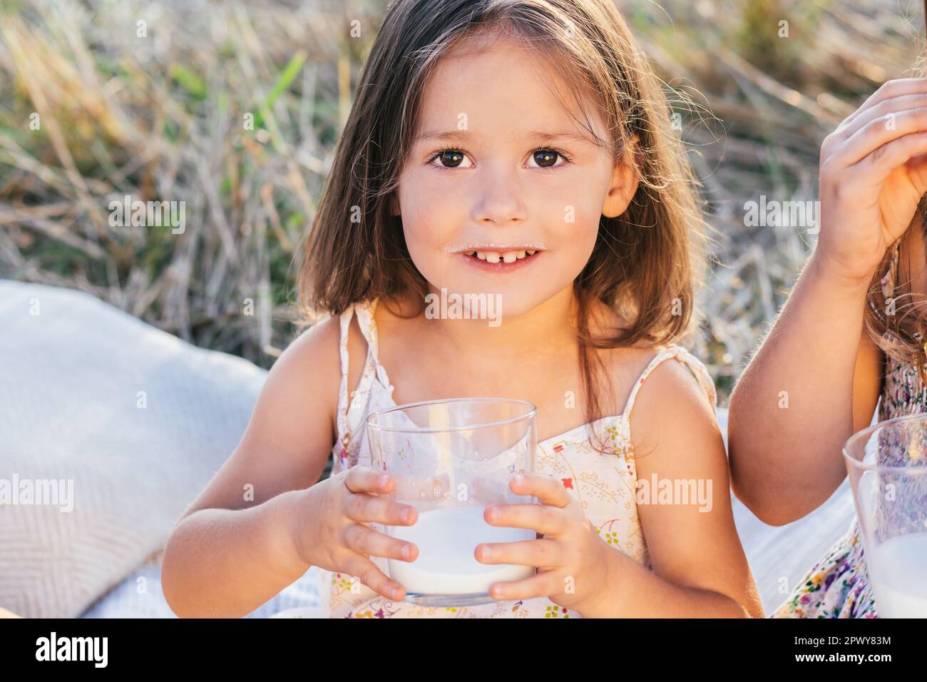 Portrait of delightful little girl looking at camera holding glass of