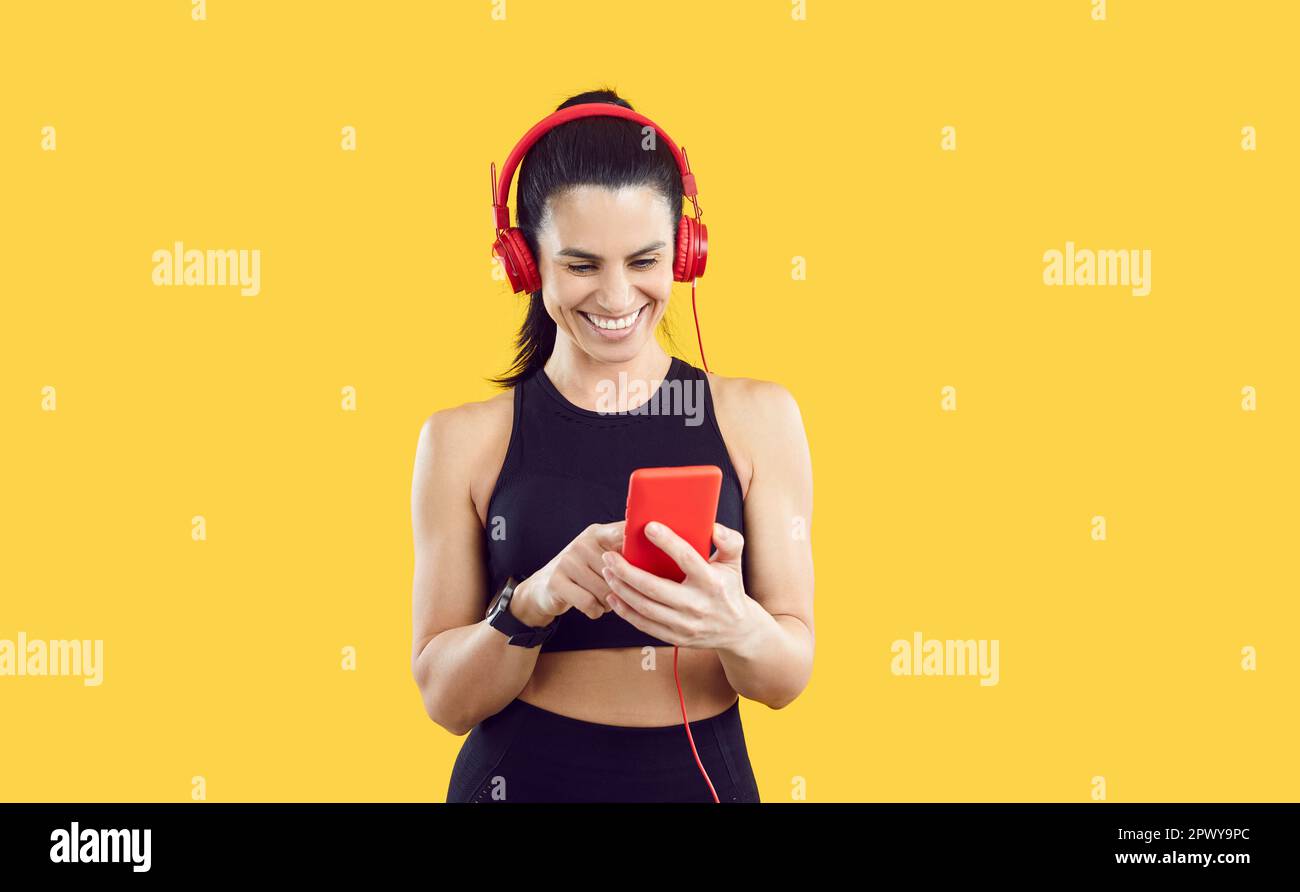 Joyful sports woman in headphones on mobile phone chooses her favorite track for sports training. Stock Photo