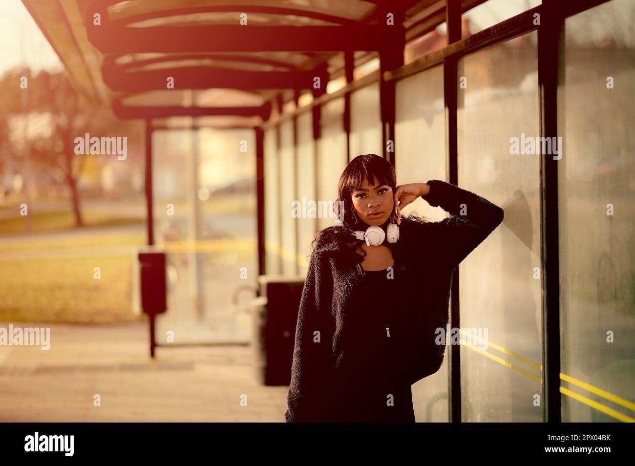 Portrait of young attractive woman in black clothes waiting for the bus at bus stop,, Urban portrait of young confident woman at bus stop wearing blac Stock Photo