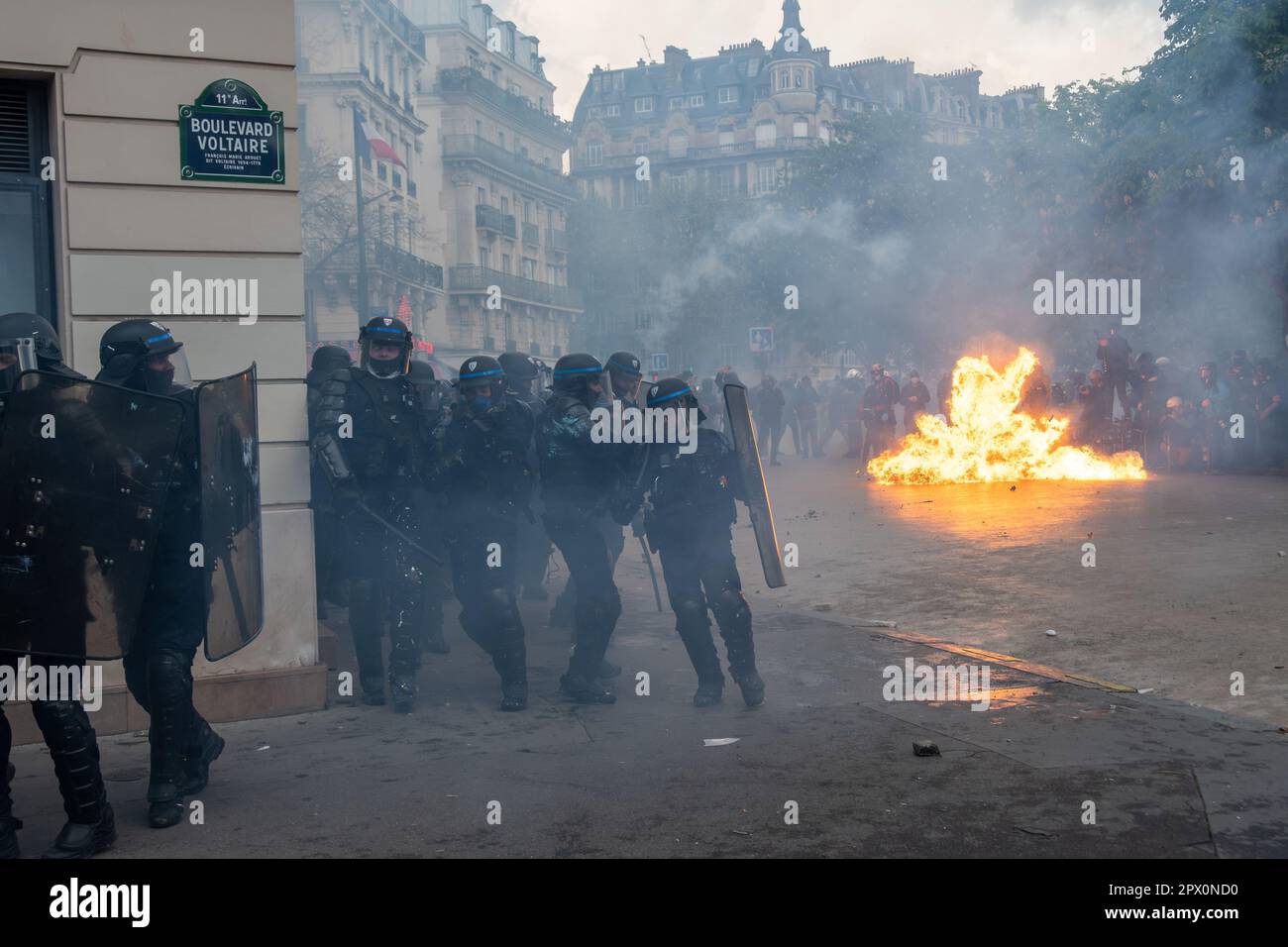 French riot police (CRS) momentarily retreating while many rioters set urban furniture on fire at the end of a protest against the retirement reform Stock Photo